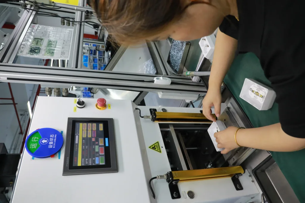 A technician checking a bank of green ageing test cabinets with extraction ducts in a room labelled Aging Zone