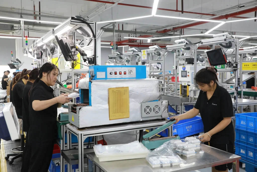 Worker inspecting a labelling and packing station on an assembly line at the Changzhou factory, with packed cartons in the background