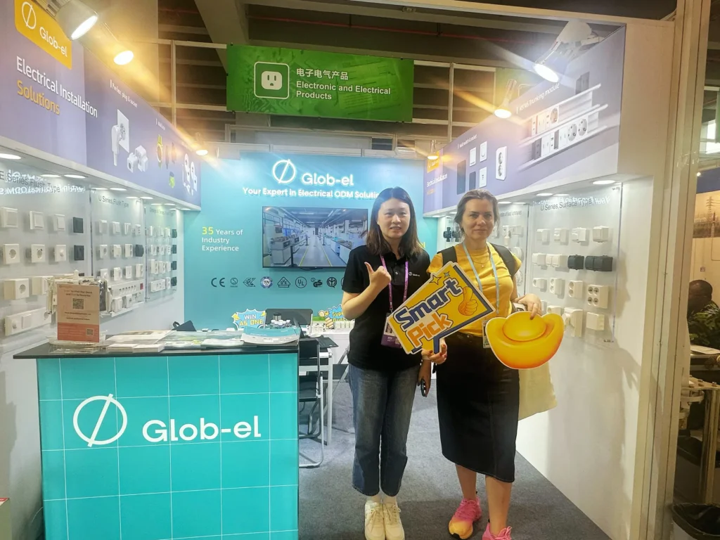 The Glob-el stand at Canton Fair 2025, showing installation boxes, switches and sockets on display with staff and a visitor