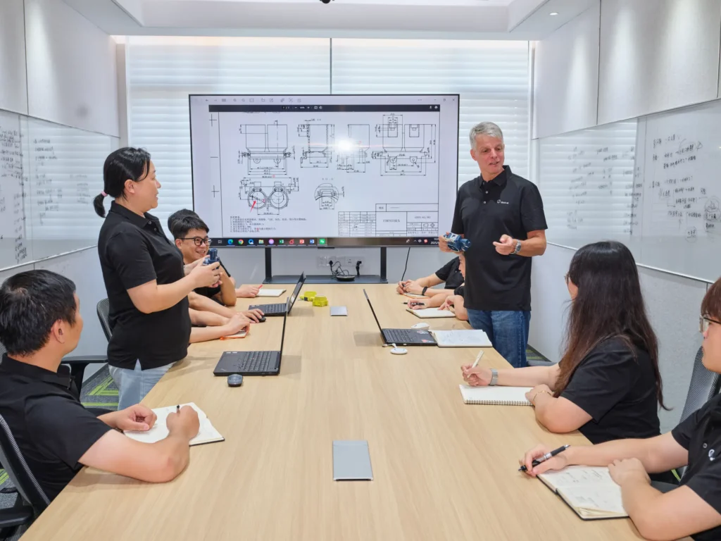 Chinese and European engineering team members reviewing a technical drawing for a connector part in a meeting room