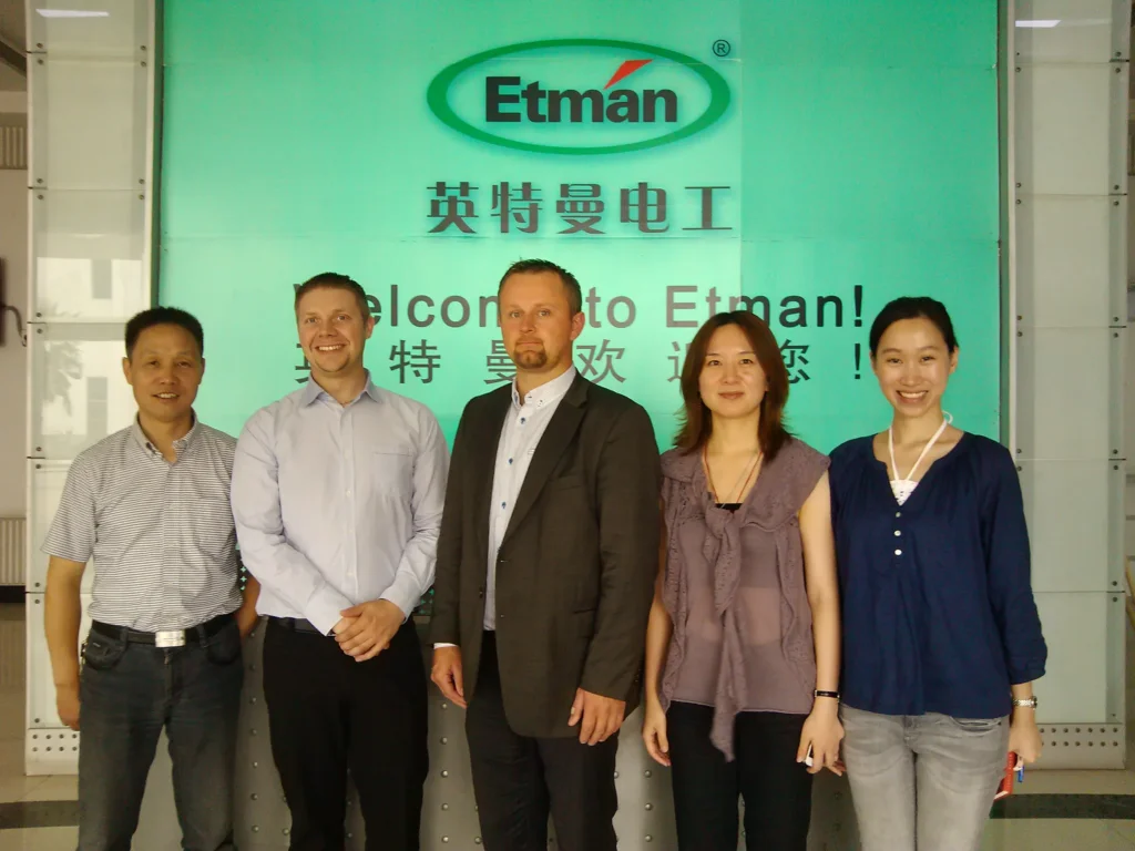 International visitors and Etman Electric staff posing together in front of a Welcome to Etman sign at the factory