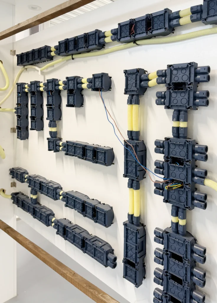 Multiple Glob-el hollow and timber wall installation boxes ganged together and mounted on a stud-frame wall before plastering, linked by yellow corrugated conduit