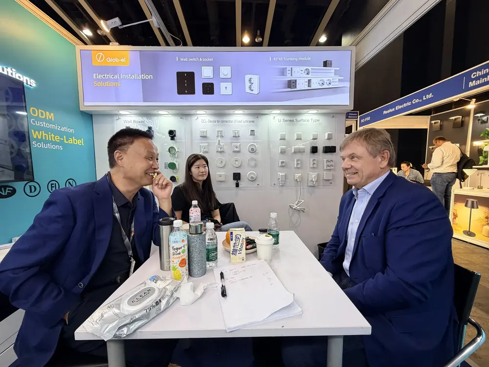 Glob-el booth at the Hong Kong Lighting Fair with wall switch and socket products, three people talking