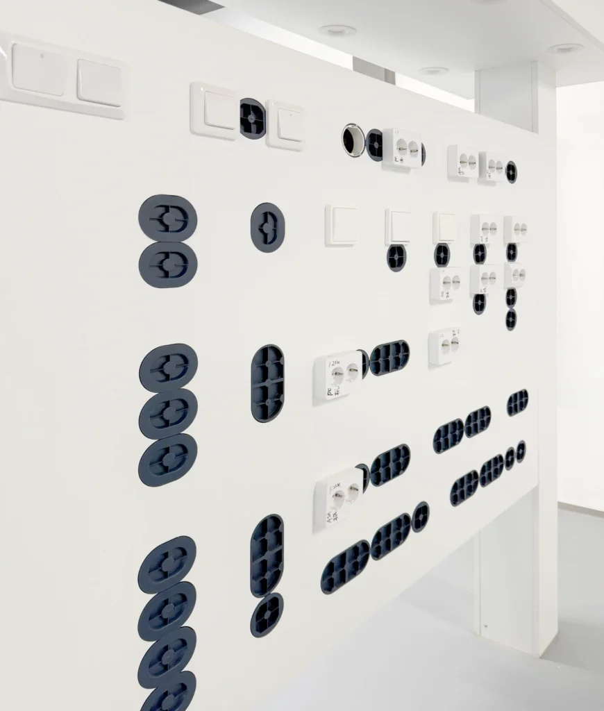 Installed switch and socket samples on a Glob-el showroom fit-test wall, several labelled with handwritten torque and fixing reference notes across different device formats